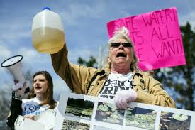 citizens rally to bring attention to the issue. One protester is pictured holding a sample of brown water that comes from the taps of Flint
